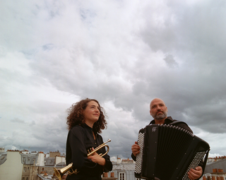 Photo des deux musiciens avec leur instrumlents sur un toit d'immeuble avec un ciel chargé en nuages en fond
