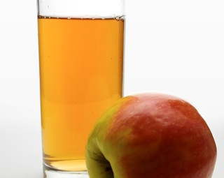 Photo d'une pomme posée devant un verre de jus de pomme
