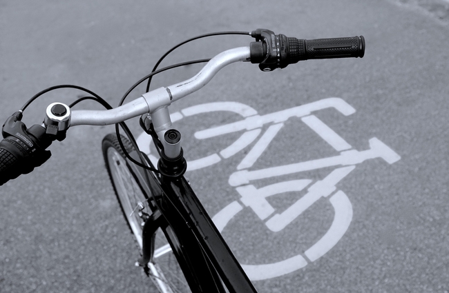 Vue du guidon d'un vélo avec en fond le visuel de la piste cyclable sur la voie