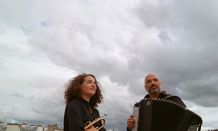 Photo des deux musiciens avec leur instrumlents sur un toit d'immeuble avec un ciel chargé en nuages en fond
