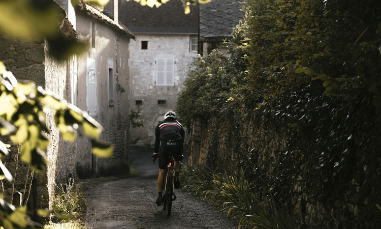 Un cycliste vu de dos sur un chemin à l'entrée d'un village