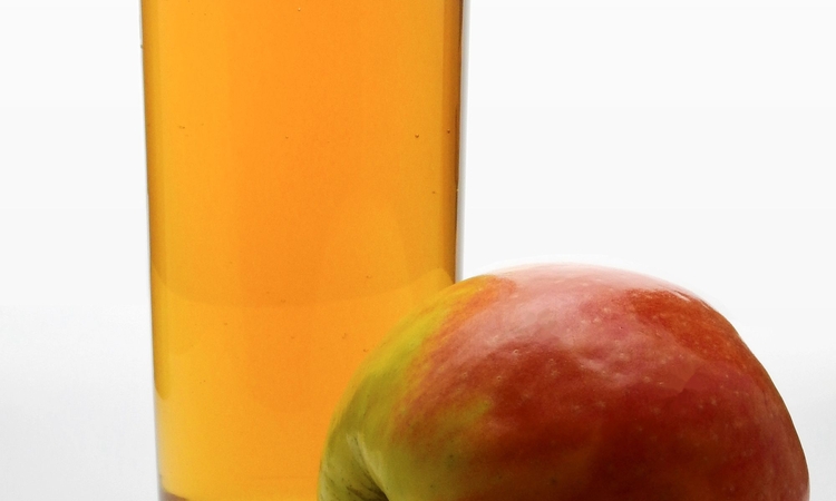 Photo d'une pomme posée devant un verre de jus de pomme