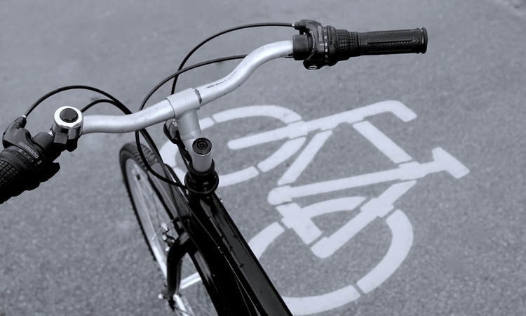 Vue du guidon d'un vélo avec en fond le visuel de la piste cyclable sur la voie